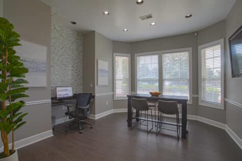 Bright business center at Emerald Lakes in Greenwood, Indiana, with expansive windows, a collaborative high-top table, built-in computer station, modern gray finishes, and contemporary furnishings by HILLS Properties.
