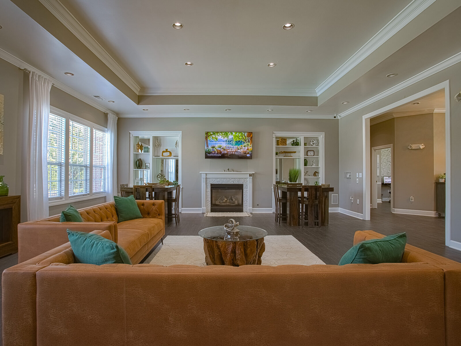 Spacious resident clubhouse at Emerald Lakes in Greenwood, Indiana, showcasing cozy lounge seating, a fireplace entertainment area, high ceilings with recessed lighting, and stylish community dining spaces by HILLS Properties.