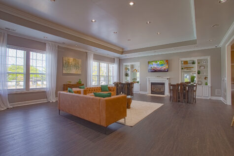 Contemporary clubhouse lounge at Emerald Lakes in Greenwood, Indiana, featuring modern leather seating, a fireplace with mounted TV, large sunlit windows, and upscale community gathering spaces by HILLS Properties.