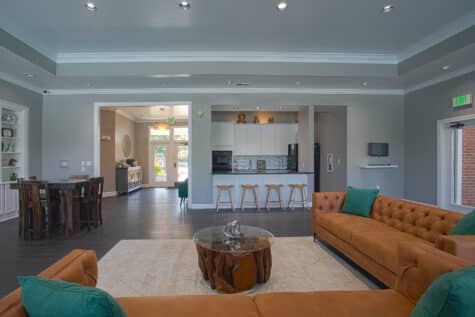 Stylish clubhouse lounge at Emerald Lakes in Greenwood, Indiana, with modern leather sofas, a contemporary kitchen bar area, high ceilings, and upscale resident social spaces by HILLS Properties.