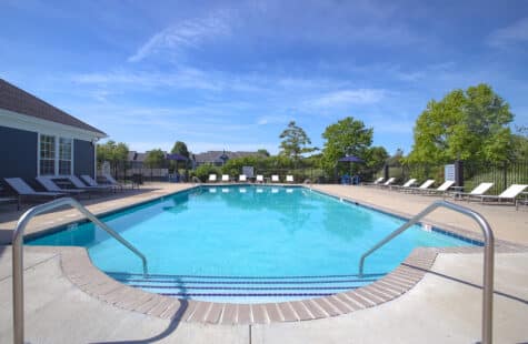 Scenic swimming pool at Emerald Lakes in Greenwood, Indiana, showcasing wide entry steps, poolside lounge seating, landscaped surroundings, and resort-inspired amenities by HILLS Properties.