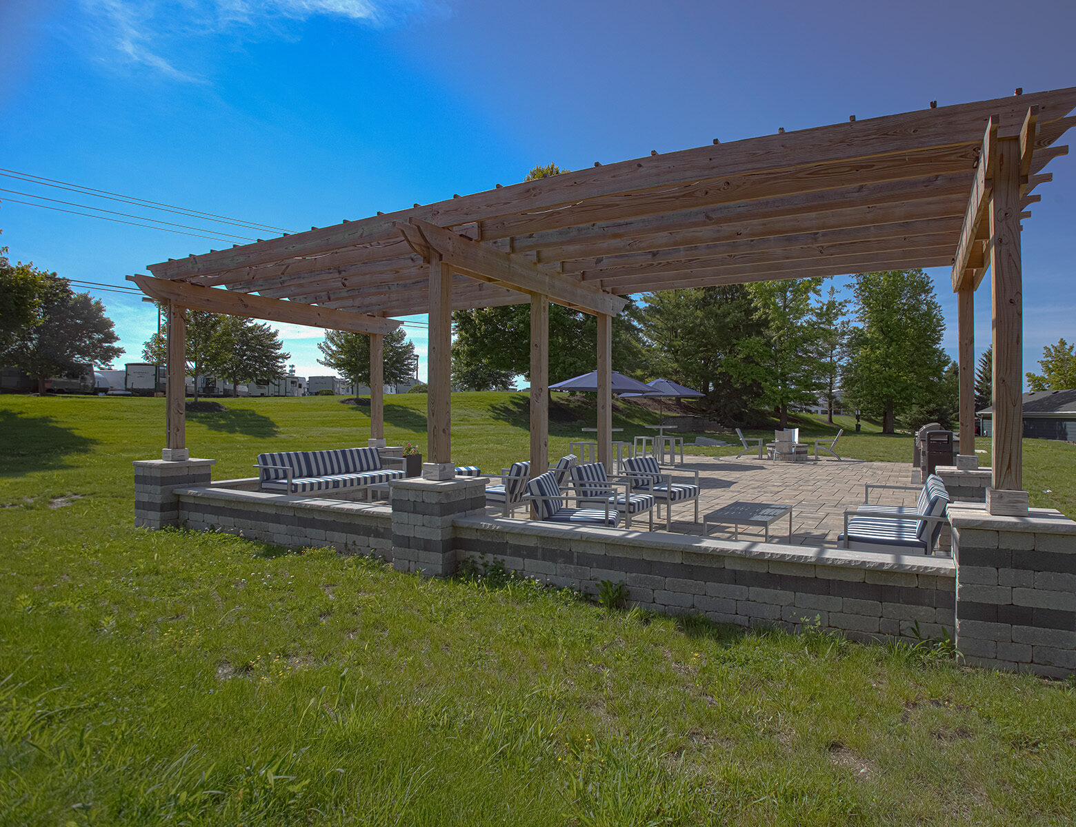 Outdoor pergola lounge area with cushioned seating, patio tables with umbrellas, and landscaped green space designed for community relaxation and gathering.