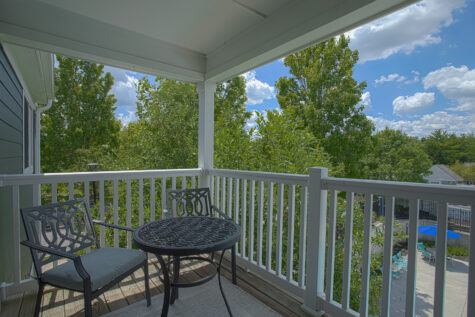 Private covered balcony at Island Club by HILLS Properties in Maineville, Ohio, featuring bistro seating with peaceful views of mature trees and the community pool.