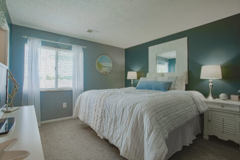 Spacious primary bedroom at Island Club by HILLS Properties in Maineville, Ohio, featuring plush carpeting, a large window with natural light, a stylish accent wall, and contemporary furnishings.