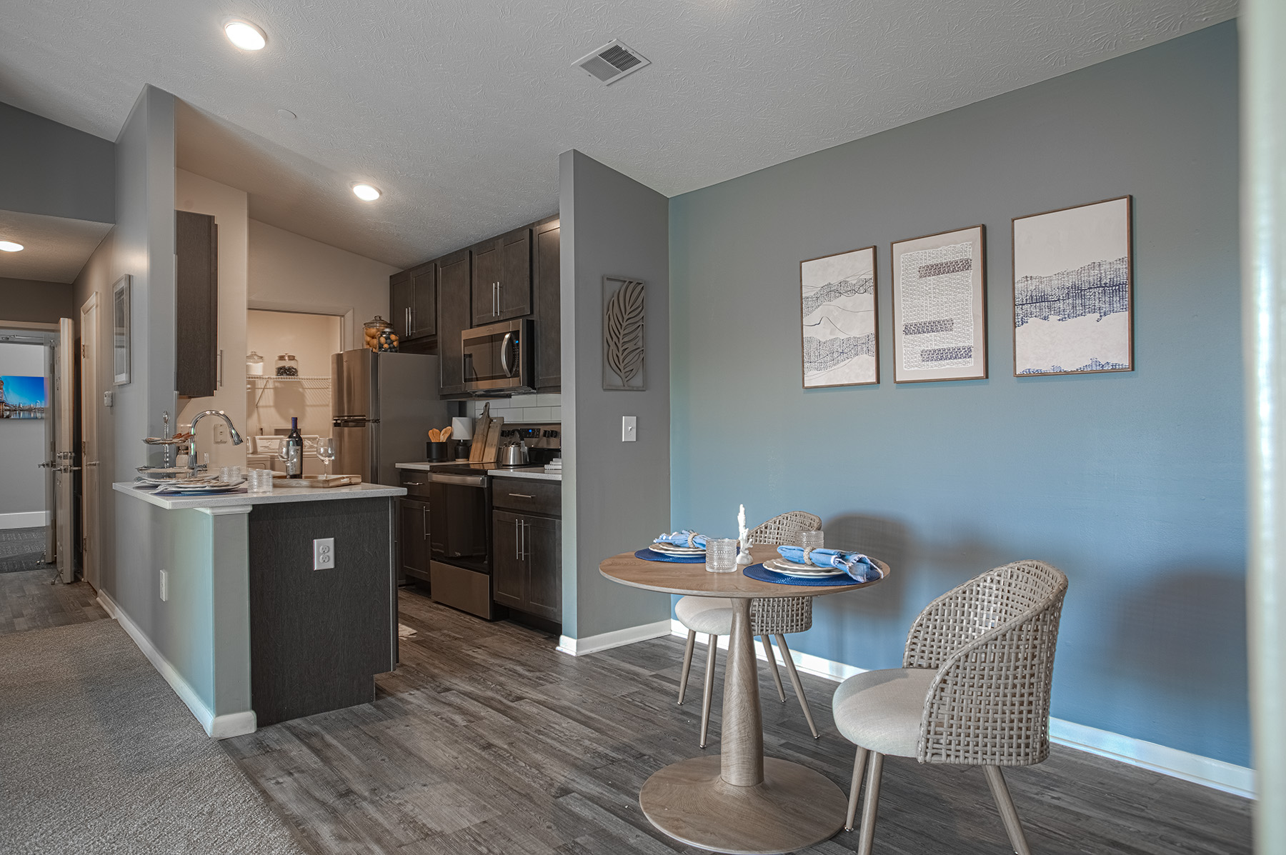 Open-concept kitchen and dining area at Island Club by HILLS Properties in Maineville, Ohio, showcasing stainless steel appliances, dark cabinetry, a breakfast bar, luxury vinyl plank flooring, and a cozy dining space.