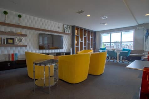 Upscale community lounge at Savoy at The Streets of West Chester in West Chester, Ohio, showcasing a media wall, built-in shelving, modern seating, and collaborative workspaces designed by HILLS Properties.