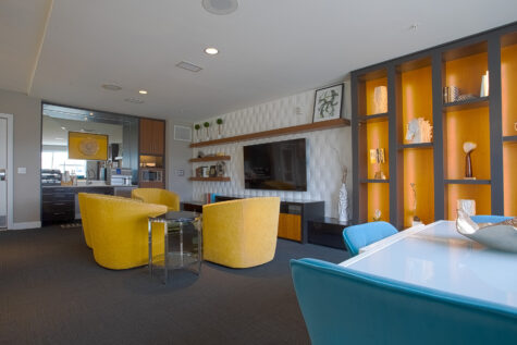 Contemporary resident lounge and workspace at Savoy at the Streets of West Chester in West Chester, Ohio, featuring yellow accent chairs, built-in shelving, media wall, and collaborative seating areas by HILLS Properties.