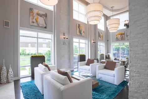 Modern apartment clubhouse lounge at Savoy at the Streets of West Chester in West Chester, Ohio, featuring white lounge seating, tall windows, contemporary lighting, and upscale décor by HILLS Properties.