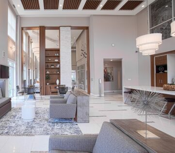 Contemporary clubhouse lounge at Savoy at the Streets of West Chester in West Chester, Ohio, featuring stylish gray seating, open-concept design, tall windows, and upscale resident amenities by HILLS Properties.