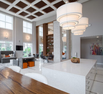 Luxury resident clubhouse at Savoy at the Streets of West Chester in West Chester, Ohio, featuring soaring ceilings, designer lighting, modern lounge seating, and a spacious kitchen island by HILLS Properties.