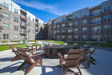Spacious courtyard at Vantage Anderson by HILLS Properties in Anderson, Ohio, featuring Adirondack seating surrounding a large fire pit, landscaped green space, and contemporary apartment buildings.