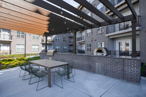 Covered outdoor social deck at Vantage Anderson by HILLS Properties in Anderson, Ohio, with a pergola, community dining table, built-in gas grill, pizza oven, and modern courtyard views.
