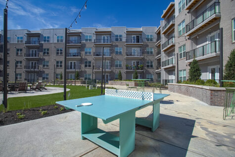 Outdoor recreation area at Vantage Anderson by HILLS Properties in Anderson, Ohio, featuring a ping pong table, landscaped courtyard, lawn games, and modern apartment buildings with private balconies.