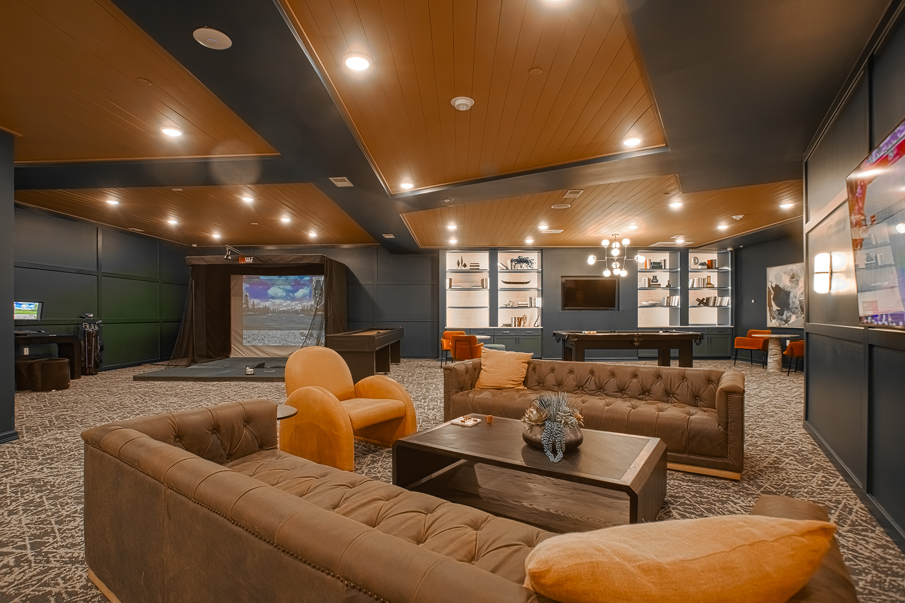 Spacious resident clubhouse at Vantage Anderson in Anderson, Ohio, featuring comfortable lounge seating, a pool table, built-in shelving, and a golf simulator entertainment area by HILLS Properties.