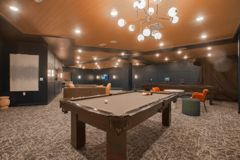 Resident game room at Vantage Anderson in Anderson, Ohio, with a billiards table, modern lounge seating, golf simulator, and contemporary lighting by HILLS Properties.