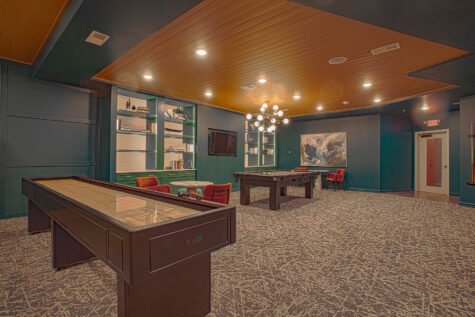 Alt text: Resident game lounge at Vantage Anderson by HILLS Properties in Anderson, Ohio, showcasing shuffleboard, a pool table, built-in shelving, contemporary seating, and stylish finishes for socializing and recreation.