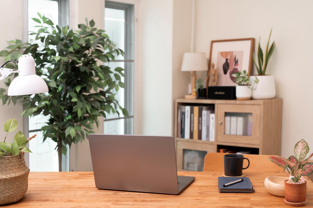 A stylish and bright home office workspace featuring a laptop on a wooden desk with abundant plants and minimalist decor.