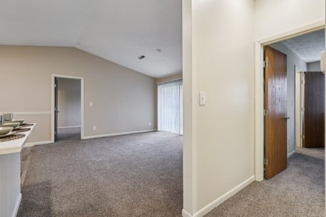 Spacious living room in the Hunter floor plan at Fox Chase North Apartments with plush carpeting, vaulted ceilings, and sliding glass doors for natural light.