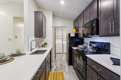 Modern galley-style kitchen with quartz countertops, subway tile backsplash, black appliances, and generous cabinet storage.