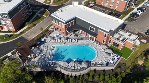 Aerial view of the resort-style swimming pool and clubhouse at Relay 129 Apartments and Townhomes in Liberty Township, Ohio, featuring expansive sundecks, shaded pergolas, and outdoor lounge spaces.