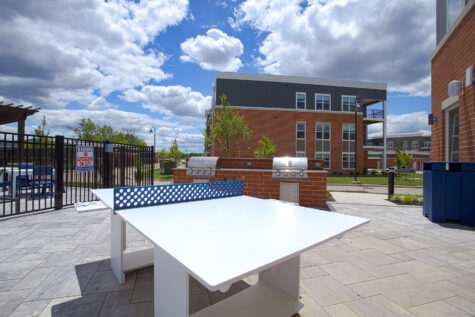Outdoor social deck at Relay 129 Apartments and Townhomes featuring a ping pong table, built-in grilling stations, and gathering spaces designed for resident entertainment.