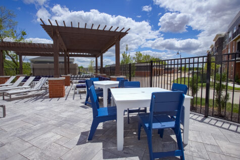 Covered outdoor social deck at Relay 129 Apartments and Townhomes featuring dining tables, comfortable seating, and a shaded pergola overlooking the community.