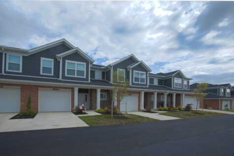 Row of modern townhomes at Relay 129 Apartments and Townhomes in Liberty Township, Ohio, with attached garages, covered entrances, manicured landscaping, and spacious driveways.