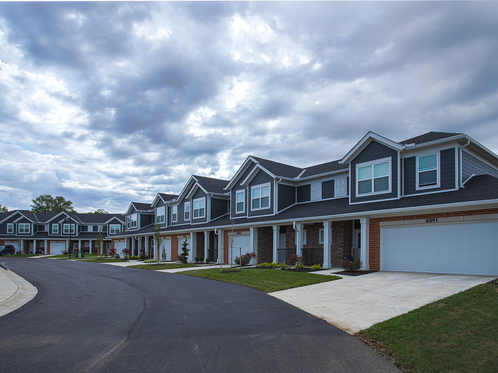 Modern townhomes at Relay 129 Apartments and Townhomes in Liberty Township, Ohio, featuring attached garages, covered front porches, landscaped lawns, and a quiet residential streetscape.