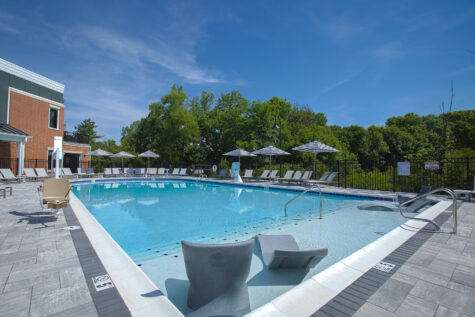 Resort-style swimming pool at Relay 129 Apartments and Townhomes in Liberty Township, Ohio, featuring a tanning shelf with in-water loungers, expansive sun deck, and modern clubhouse views.