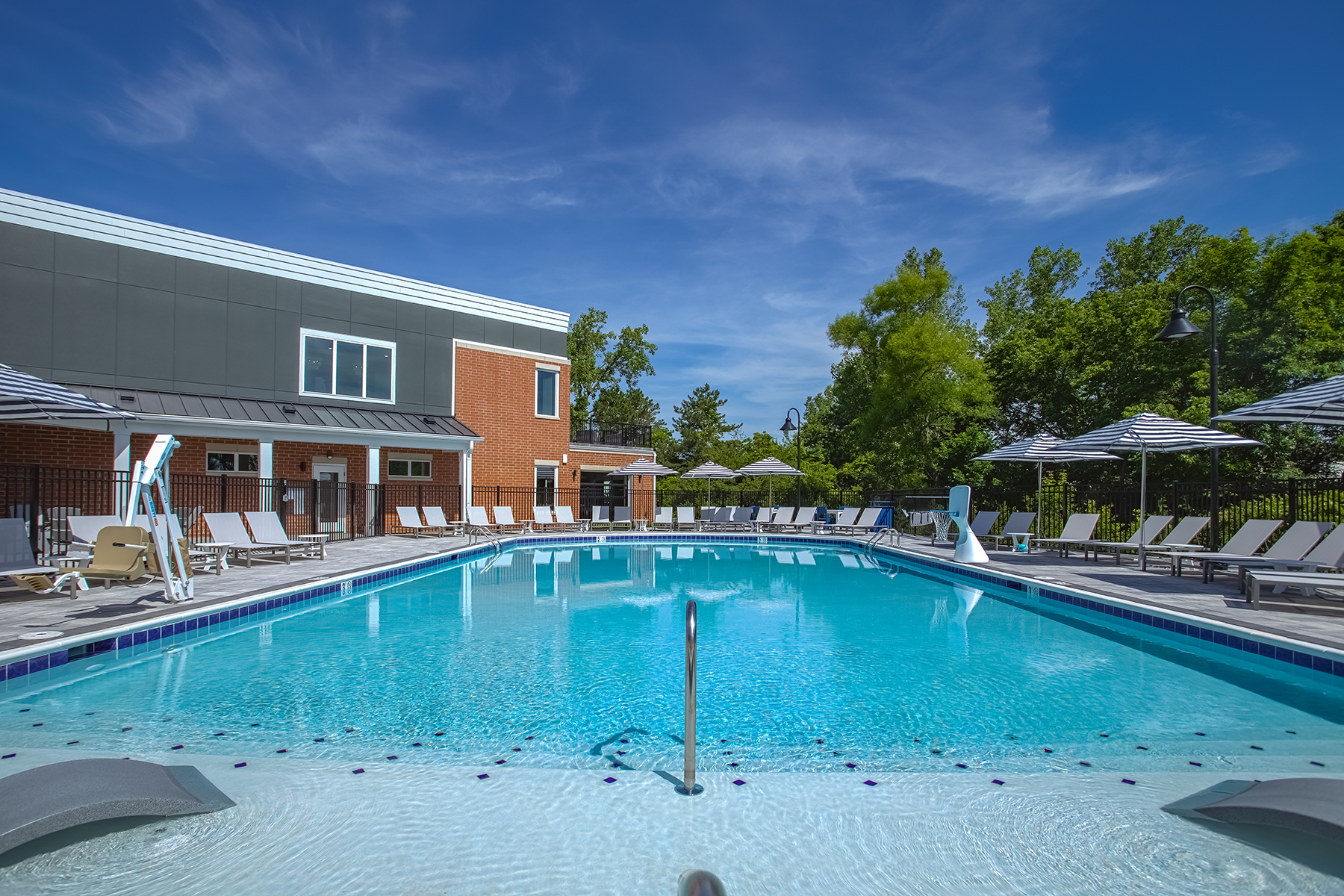 Luxury swimming pool at Relay 129 Apartments and Townhomes showcasing a tanning ledge with in-water loungers, spacious pool deck seating, and a modern clubhouse backdrop.